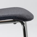 Close-up van moderne gestoffeerde stoel, met een slank verchroomd metalen frame en donkergrijze geweven stof.