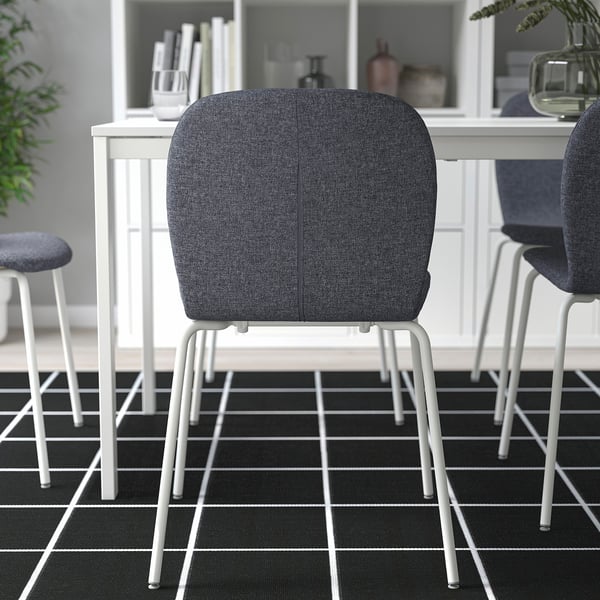 Twee moderne stoelen in de buurt van witte tafel met vaas en boeken. Zwart/wit vloerkleed op de vloer.