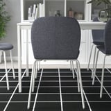 Twee moderne stoelen in de buurt van witte tafel met vaas en boeken. Zwart/wit vloerkleed op de vloer.