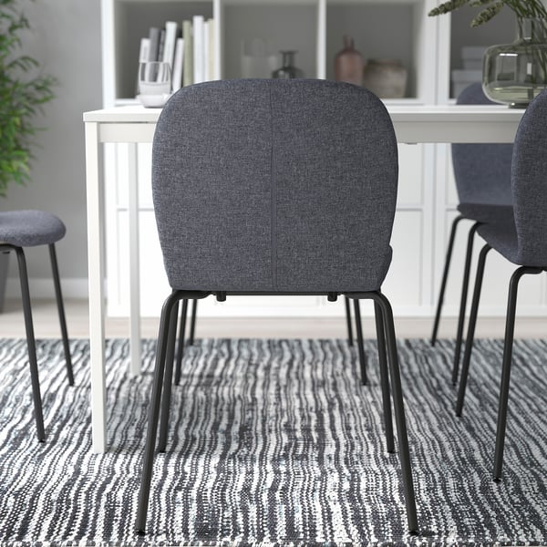 Donkere gestoffeerde bureaustoel met metalen poten op een gedessineerd tapijt, in een kamer met witte meubels.