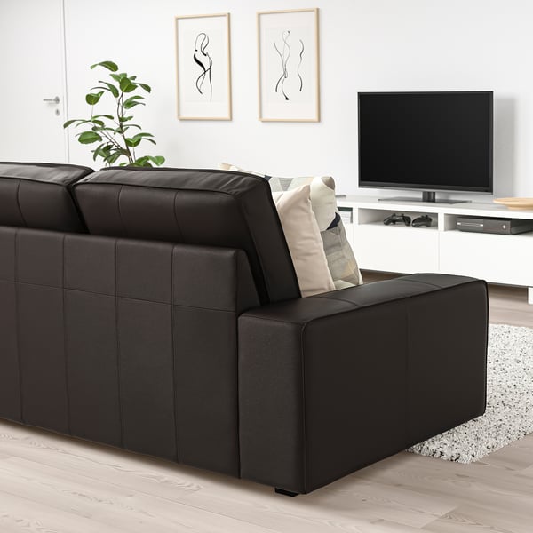 Moderne woonkamer met grote KIVIK zwarte leren bank, geometrische kussens, flatscreen-tv en abstracte kunst aan de muur.