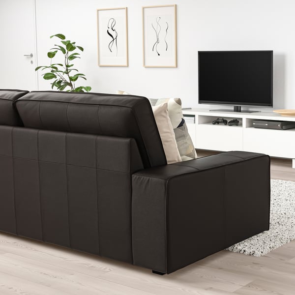Moderne woonkamer met grote zwarte leren KIVIK bank, wit tv-meubel en abstracte kunst aan de muur. De grootte van de banken domineert de ruimte.