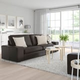 Moderne woonkamer met een ruime, donkergrijze KIVIK bank, lichte kussens, houten tafels en grote ramen.