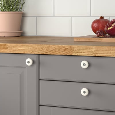 Aanrecht met grijze laden, houten blad, witte knoppen, granaatappels en plant.