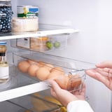De hand plaatst duidelijke plastic eierdoos in koelkast, houdend transparant deksel, die georganiseerde opslag tonen.