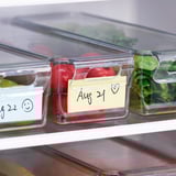 Doorzichtige plastic koelkastcontainers met deksels, gelabeld met datums, bewaren en organiseren voedsel efficiënt.