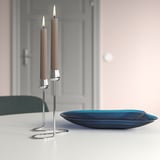 Zilveren kandelaar met beige kaarsen en spiraalvoet op tafel naast donkerblauwe glasplaat.