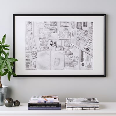 Ingelijste collagekunst met paspoortstempels die op een plank worden getoond, vergezeld van boeken en een plant.