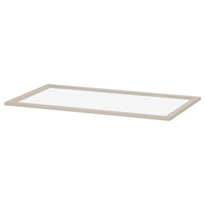 Een ikea KOMPLEMENT glazen plank, helder en rechthoekig, omlijst in lichtbeige. Het is gemaakt van hardboard en gehard glas, ontworpen voor pax kledingkasten.