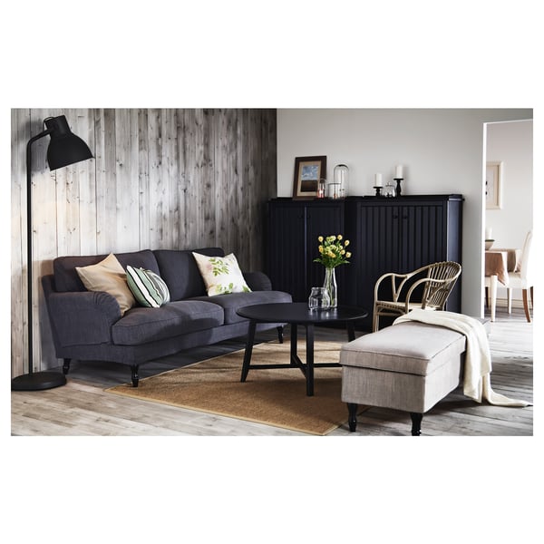 Zwarte salontafel met houten poten, ronde vorm. Gedecoreerd met een vaas met bloemen en geplaatst in een stijlvolle woonkamer.