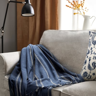 KRUTBRÄNNARE blauwe plaid op grijze bank. Dobby streep weefsel, zacht katoen, driehoekige vouw, decoratie op rechter armleuning.