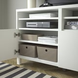 Wit kabinet met open deur, met georganiseerde planken. Inclusief grijze dozen, stapels papieren en elektronische items.