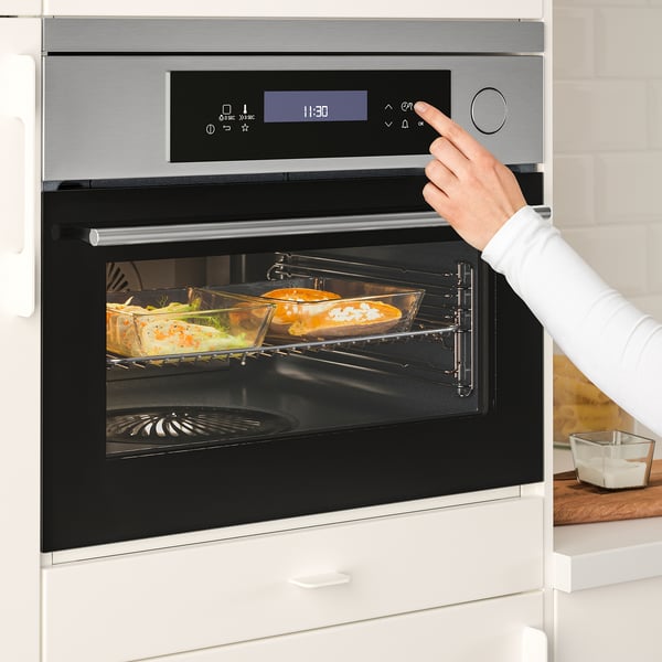 Persoon die de digitale vertoning van moderne ovens aanpast terwijl het voedsel binnen kookt.