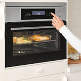 Persoon die de digitale vertoning van moderne ovens aanpast terwijl het voedsel binnen kookt.