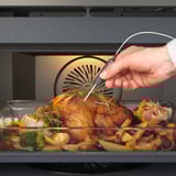 De hand steekt de vleesthermometer in de geroosterde kip in de oven, wat zorgt voor nauwkeurig koken.
