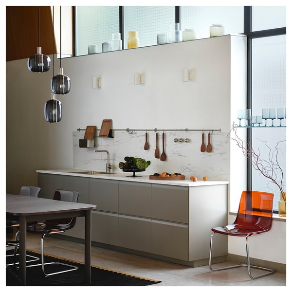 Moderne keuken met grijze kasten, marmeren achterwand, hangend houten keukengerei, roestvrijstalen rail, oranje stoel.