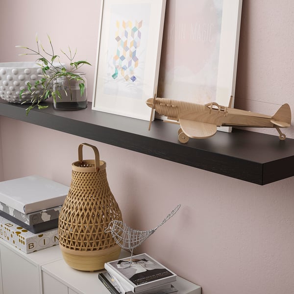 Een wandplank met decoratieve voorwerpen: een modelvliegtuig, boeken en een mand. De beugels zijn verborgen, waardoor de plank in de muur opgaat.