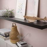 Een wandplank met decoratieve voorwerpen: een modelvliegtuig, boeken en een mand. De beugels zijn verborgen, waardoor de plank in de muur opgaat.
