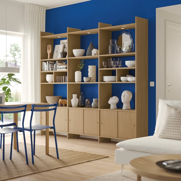 Houten opbergmeubel tegen blauwe muur met decor, stoelen, tafel en bank in een moderne leefruimte.