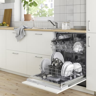 Vaatwasser open met schone vaat in lichte keuken, plant in de buurt.