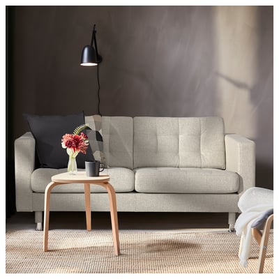 Moderne woonkamer met lichtgrijze LANDSKRONA bank, houten bijzettafel en zwarte wandlamp. Sierkussens en vaas met bloemen op tafel.