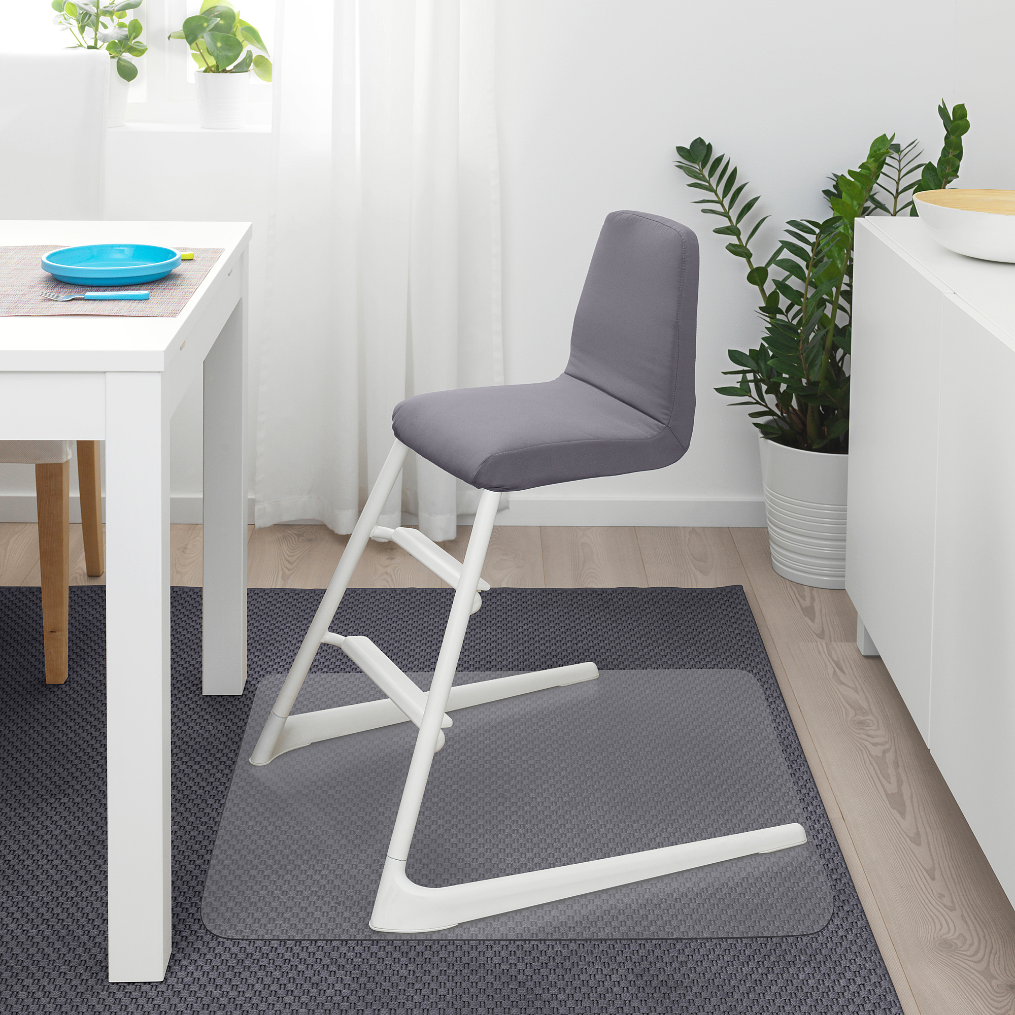 Moderne kinderstoel, grijs, witte poten, gecapitonneerde zitting. Ideaal voor kleine ruimtes naast een wit bureau en potplant.