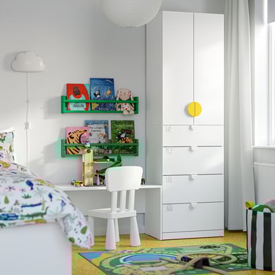 Kinderkamer met witte LASTARE-lades , een klein stoeltje en kleurrijke boeken. Grijze muren, levendig tapijt, gezellig leeshoekje.