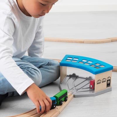 Kind spelen met LILLABO treinset. Ze duwen een groene trein op rails in de buurt van een blauw station.