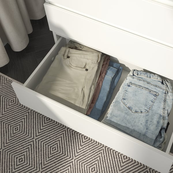 Open witte lade die netjes opgevouwen broek in verschillende kleuren onthulde op een tapijt met patroon