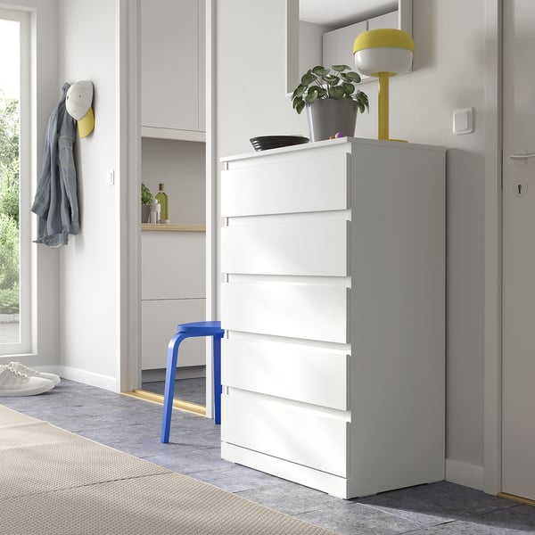 Witte LILLBERGET-ladekast in de woonruimte met een blauwe kruk, gele lamp en groene plant erbovenop, naast een deur.