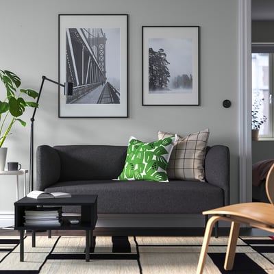 Grijze LILLEHEM bank met groene kussens, zwarte salontafel en planten.