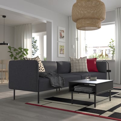 Moderne woonkamer met LILLEHEM bank, kussens, salontafel, groot raam, rieten licht, gestreept vloerkleed en wanddecoratie.