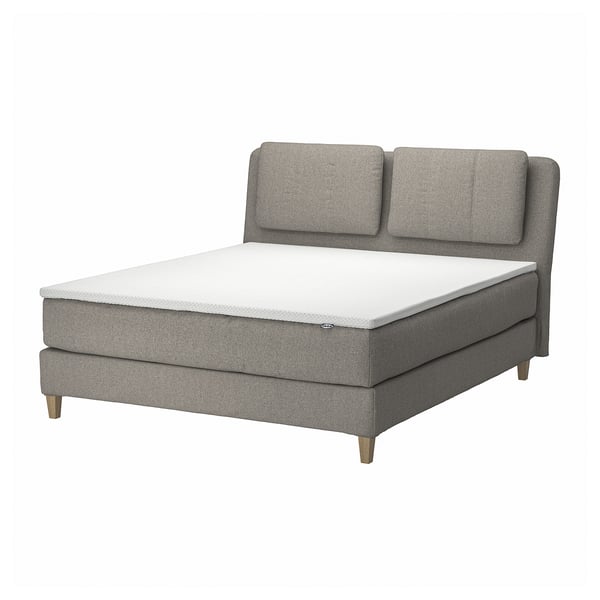 Modern grijs stoffen bed met kussens, houten poten en witte matras.