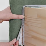 Persoon die de hoes met klittenband vasthoudt en aan het groene bedframe bevestigt.