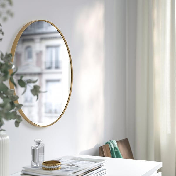 De spiegel op witte muur weerspiegelt de bouw. Tafel met vaas, parfum, armband en tijdschriften eronder.