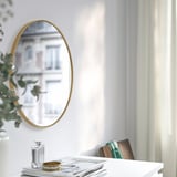 De spiegel op witte muur weerspiegelt de bouw. Tafel met vaas, parfum, armband en tijdschriften eronder.