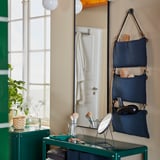 Moderne badkamer met LINDBYN-spiegel met zwarte lijst, hangende marineblauwe opbergruimte, groene ijdelheid, make-upbenodigdheden en potplanten.