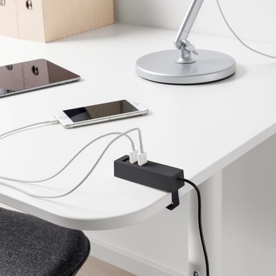 Een slanke zwarte USB-oplader staat op een wit bureau en bevat drie aangesloten witte kabels die een smartphone en andere apparaten van stroom voorzien.