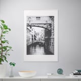 Ingelijste kanaalscène met brug, plankhoudende plant, vaas, kom, boeken, bol.