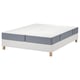 Witte bedbodem met houten poten, grijs opgerolde matrassen. Gerecycled polyester en schuim, rechthoekig.