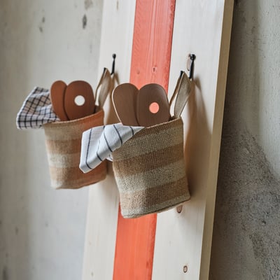 MÄVINN jute mand hangt met houten lepels aan rode en witte planken.