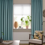 Woonkamer met MAJGULL gordijnen, stoel, plant en zacht licht.