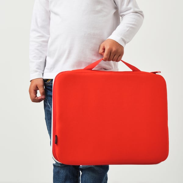 Persoon met rode MÅLA tekenkoffer met handvat, geschikt voor het dragen van kunstbenodigdheden.