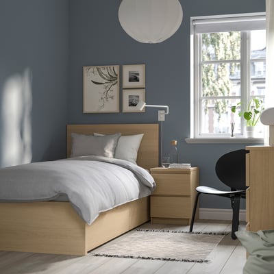 Moderne blauwe kamer met MALM-bed, licht hout, wit linnengoed. Kunst aan de muur, bureau, lamp, vloerkleed onder.