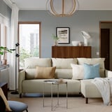 Moderne woonkamer met blauwe wand, MANNARP-bank , kussens, deken, tafel, plant en decoratieve kast met licht.