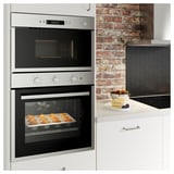 Moderne keuken met roestvrijstalen oven en magnetron, gebakken gebak, pannenkoeken en fruit op het aanrecht, bakstenen achterwand.