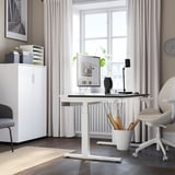 Moderne thuiskantooropstelling. MITTZON bureau met dubbele motoren, een computer, lamp en plant. Witte kast links, beige stoel rechts, maar toch ruim.