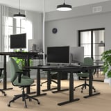 Modern kantoor met MITTZON zwarte zit-sta bureaus, groene stoelen en grote schermen. Bureaus zijn verstelbaar met dubbele motoren.