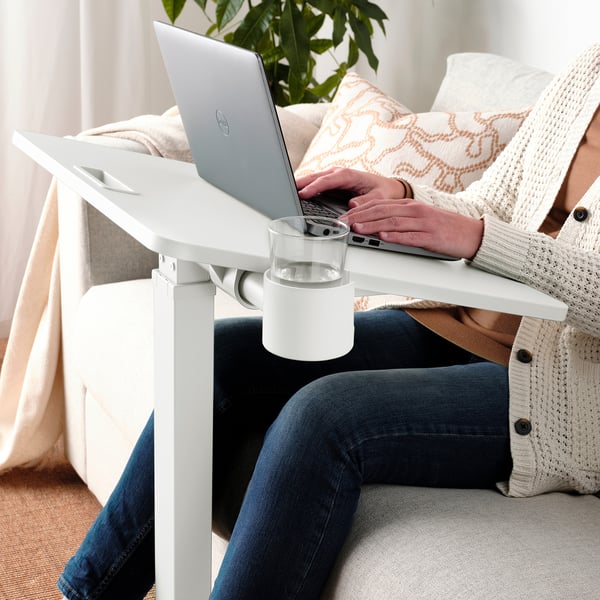 Persoon met behulp van verstelbare laptoptafel met drankje, op gezellige bank.