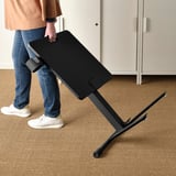 Persoon die de hoogte van de zwarte MITTZON-laptoptafel op beige tapijt aanpast, met de functionaliteit voor hoogteverstelling.